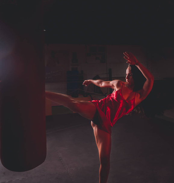An adult female in a red dress punching a punching bag with a leg - Foto, immagini
