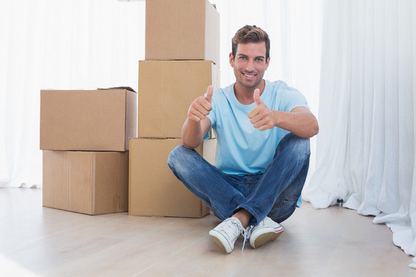 Man gesturing thumbs up with cardboard boxes in new house - Foto, Imagen