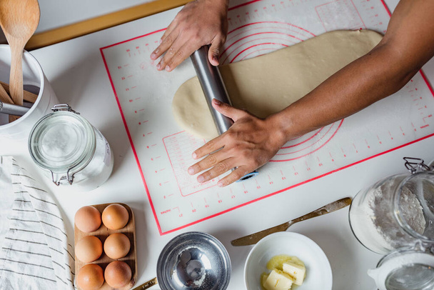 A top view shot of hands of Hispanic baker making cinnamon rolls - 写真・画像