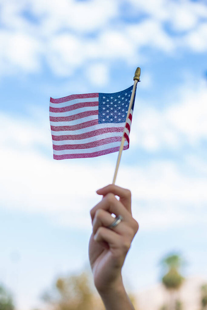 A vertical shot of a hand waving an American flag outdoors - 写真・画像