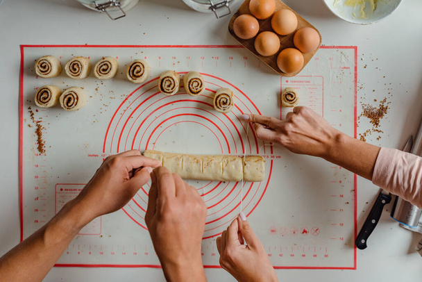 A top view shot of hands of a man and a woman preparing cinnamon rolls - Foto, immagini