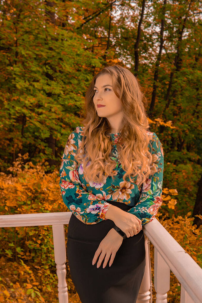 A joyful teenager stands leaning against a white railing a young blonde, in a colored shirt stands against a lake background laughing autumn perfect embrace blue eyes - Foto, immagini