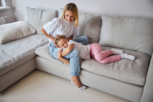 Beautiful Caucasian woman in casual clothes spending time with little girl in living room - Fotografie, Obrázek
