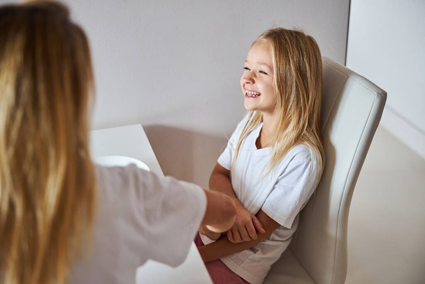Little girl laughing while talking with blonde woman in the white kitchen - Fotoğraf, Görsel