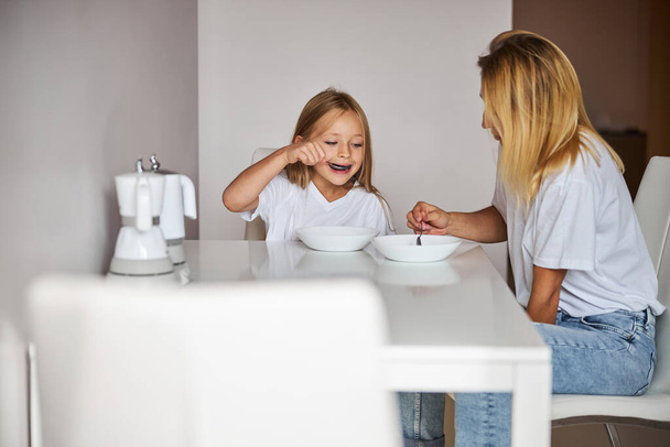 Mother and daughter having breakfast at home in kitchen - Photo, Image