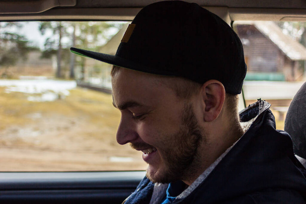 Fešák mladý chlap s vousy úsměv zatímco sedí v autě - boční pohled - Fotografie, Obrázek