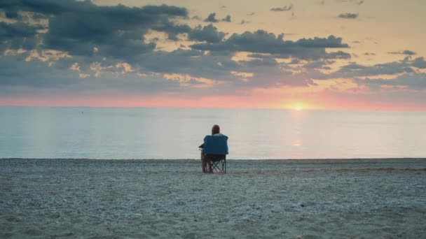 Full shot de mujer admirando puesta de sol en el mar sentado en silla de turismo plegable - Metraje, vídeo
