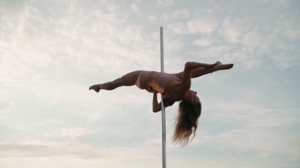 Beautiful athletic woman performs tricks on the pole against the background of sunset in the field. Beauty and body care. Female sports and fitness. Slow motion - Footage, Video