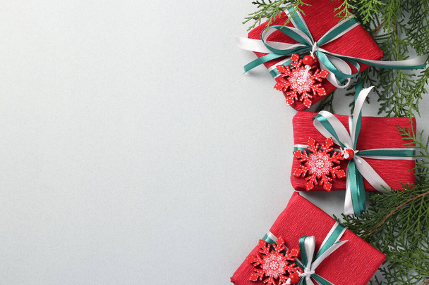 Trzy prezenty świąteczne w czerwonym papierze z płatkami śniegu i wstążkami na jasnej powierzchni. Świąteczne prezenty. Karta świąteczna. Miejsce na tekst - Zdjęcie, obraz