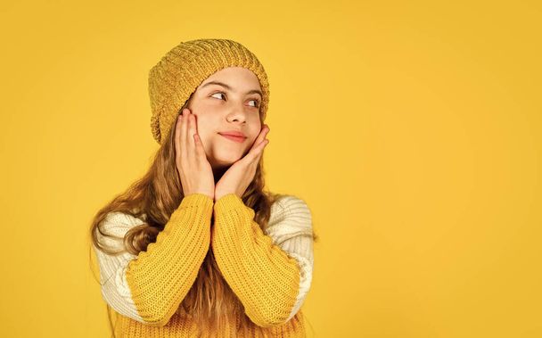 cold weather forecast. happy child wear hat and favorite sweater. copy space. teen girl yellow background. little girl in knitwear. kid beauty and fashion. get warm in winter season - Valokuva, kuva