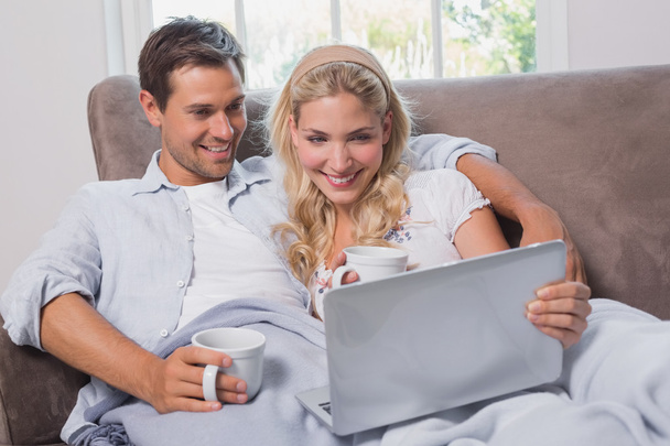 Relaxed couple with coffee cups using laptop on sofa - Fotografie, Obrázek