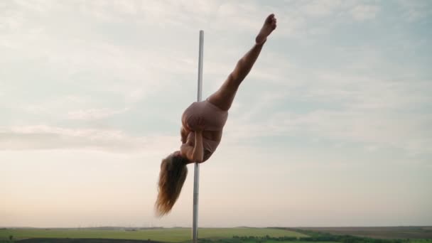 Beautiful athletic woman performs tricks on the pole against the background of sunset in the field. Beauty and body care. Female sports and fitness. Slow motion - Footage, Video