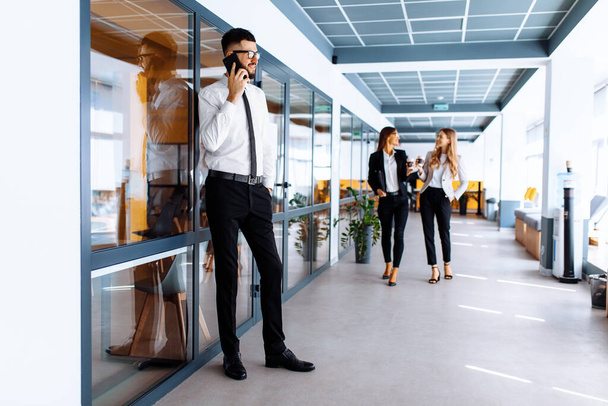 Młody, szczęśliwy biznesmen rozmawiający przez telefon komórkowy w biurze podczas przerwy - Zdjęcie, obraz