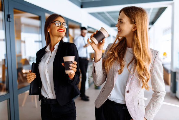 Glückliche Geschäftskollegen diskutieren etwas und trinken Kaffee, während sie den Büroflur entlang laufen. - Foto, Bild