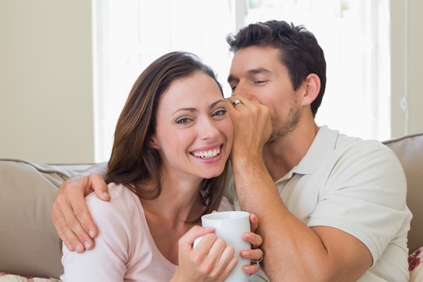 Man whispering secret into a womans ear in living room - Фото, изображение