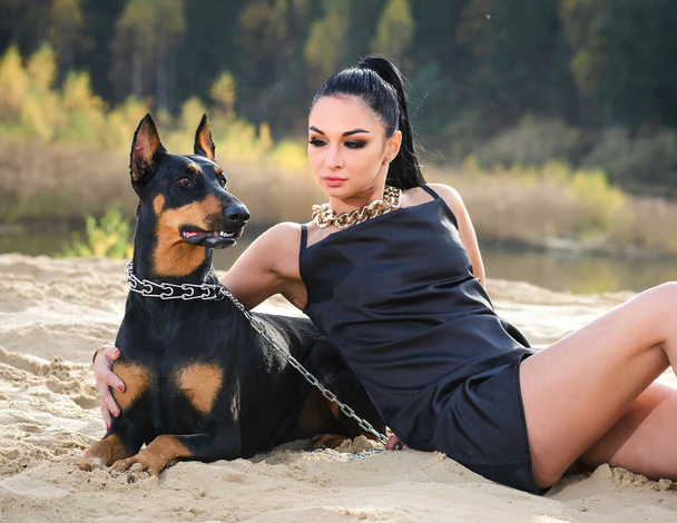A cute girl and a doberman lie on the sand in an embrace with each other. - Foto, imagen