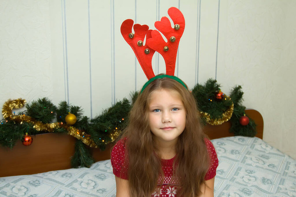 Piękny szczęśliwy 7-letnia dziewczyna nosi ładny czerwony świąteczny zespół włosów z poroża reniferów - Zdjęcie, obraz
