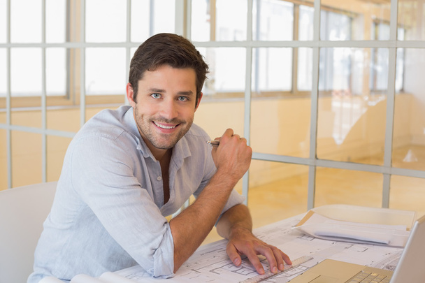Smiling businessman working on blueprints in office - Valokuva, kuva