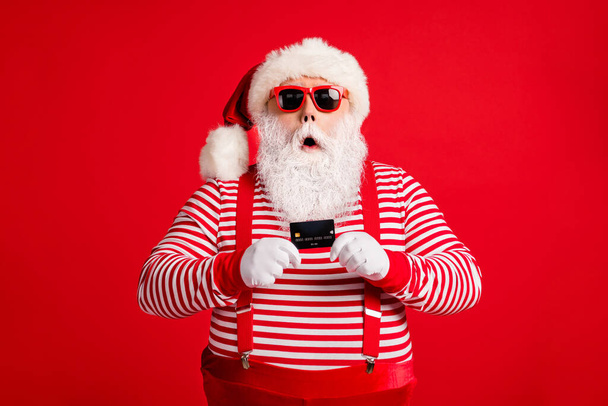 Portrait of his he nice handsome amazed stunned wondered bearded fat Santa holding in hand bank card modern novelty service reaction isolated over bright vivid shine vibrant red color background - Fotó, kép