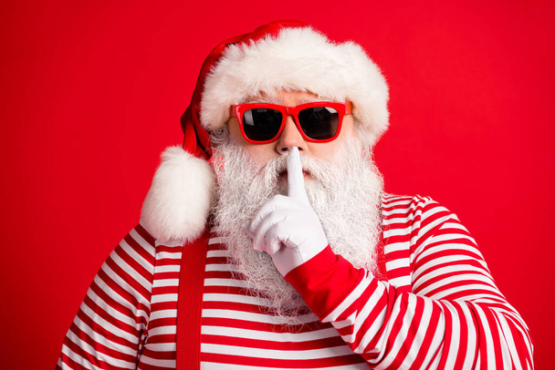 Close-up portrait of his he nice handsome mysterious white-haired Santa wearing sunglasses showing shh sign silence silent mute isolated over bright vivid shine vibrant red color background - Photo, Image