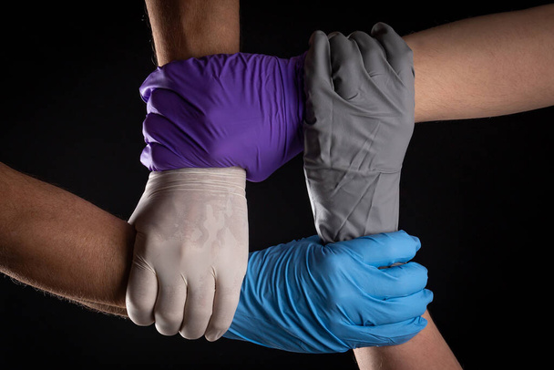 Hommes en gants de latex de différentes couleurs, tenant la main en cercle sur un fond noir. - Photo, image