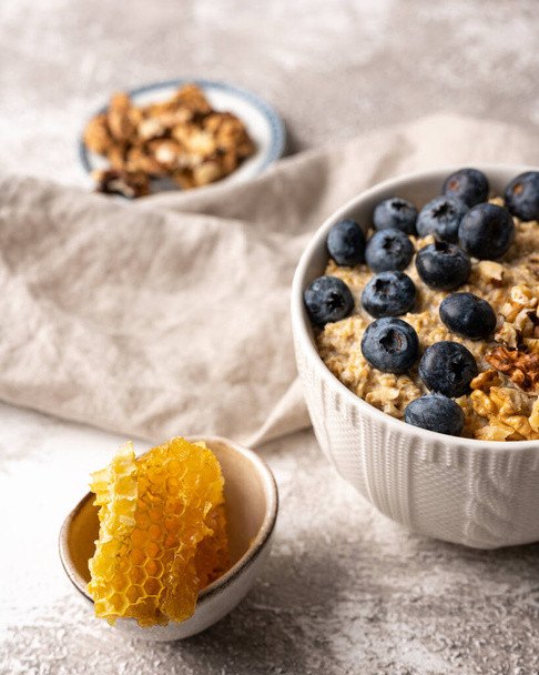 Healthy breakfast bowl: oatmeal with blueberries, nuts and honeycomb piece. Oat flakes with berries. - Photo, Image