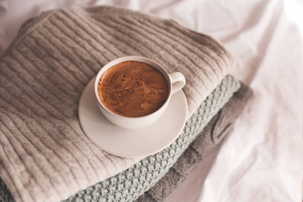 Cup of coffee with foam staying on stack of knitted sweaters close up. Good morning. Breakfast time. Winter season. - Foto, Imagem