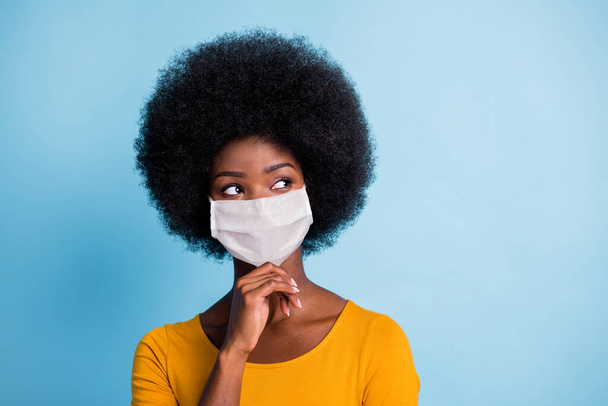 Photo of thoughtful black girl look up empty space arm chin wear mask yellow shirt isolated blue color background - Foto, imagen