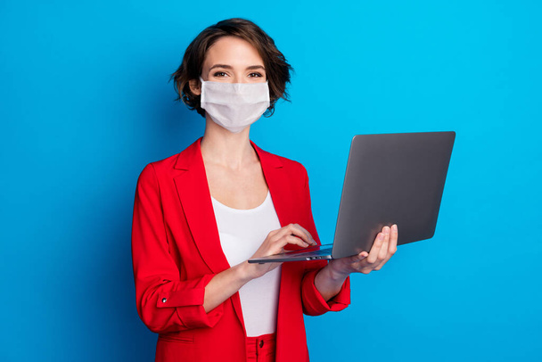 Portrait of attractive skilled business lady holding laptop wear facial protective mask isolated over blue color background - Fotó, kép