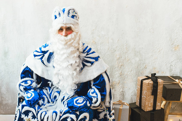 Santa Claus en un abrigo de piel azul se sienta en una habitación cálida y mira a la cámara. Año Nuevo y concepto de Navidad - Foto, imagen