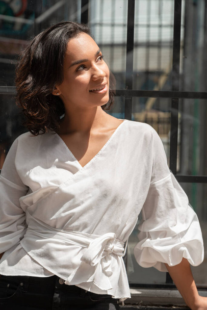 Young Latin brunette woman with short hair, distracted and smiling, wearing a white blouse, photo in the day - Fotografie, Obrázek