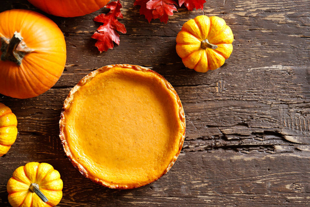 Traditional thanksgiving food on wooden table. Orange delicious homemade pumpkin pie with crust and decorative items. Thanksgiving table setting concept.Top view, close up, copy space, background. - Фото, зображення