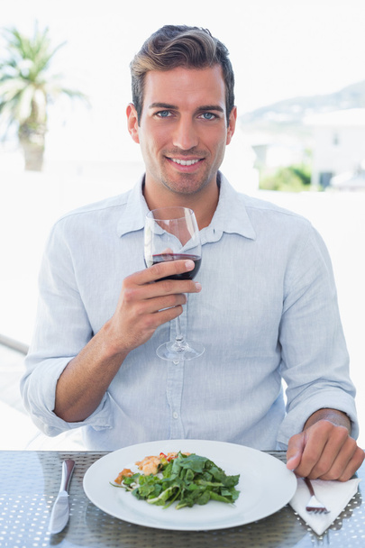 Smiling young man with wine glass having food - Фото, изображение