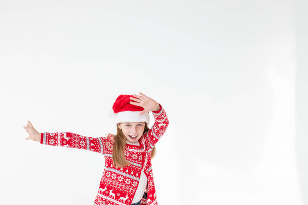 Симпатичные смешные Санты помощник танцы на белом фоне. Концепция рождественских праздников. Смешной малыш Санта. Красивая девушка в красной шляпе Санты празднует Рождество, веселится. - Фото, изображение