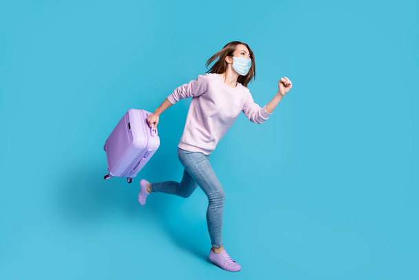 Foto lateral de perfil de longitud completa de una chica positiva corriendo sosteniendo una maleta púrpura con máscara facial azul aislada sobre fondo de color azul - Foto, Imagen