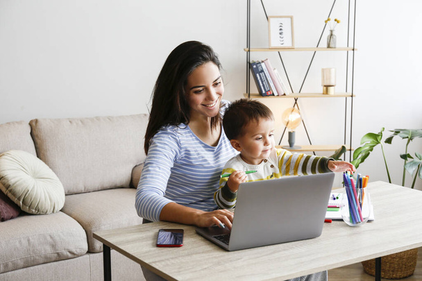 Young beautiful woman multitasking, working from home & teaching two year old son to draw. Woman spending quality time with her toddler child. Homeschooling concept. Close up, copy space, background. - Foto, imagen