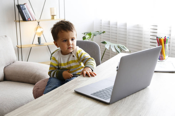 Two year old boy staring at the laptop screen with fascinated facial expression. Toddler boy sitting by the table at home with notebook computer. Close up, copy space, background. - Fotografie, Obrázek