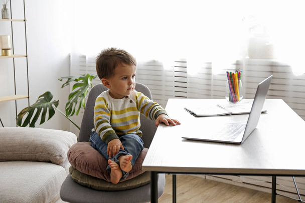 Two year old boy staring at the laptop screen with fascinated facial expression. Toddler boy sitting by the table at home with notebook computer. Close up, copy space, background. - 写真・画像