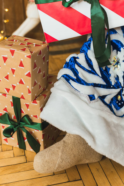 Близкий снимок ботинок Деда Мороза. Санта-Клаус в синем шубе сидит в рождественском интерьере на фоне рождественской елки - Фото, изображение