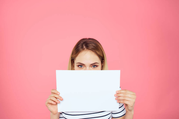 Nainen tilalla valkoinen arkki käsissään raidallinen t-paita tunteita vaaleanpunainen tausta - Valokuva, kuva
