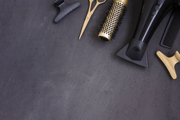 Hairdressing tools in black and gold on a gray concrete background. Hair salon accessories, hair dryer, combs, scissors and hair clips in the corner and with copy space. Template for business cards. - Photo, Image
