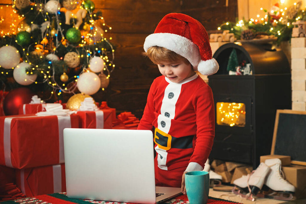 Santa helper using notebook. Child type letter to Santa. Portrait of cute dreamy Santa helper writing letter to Santa Claus - 写真・画像
