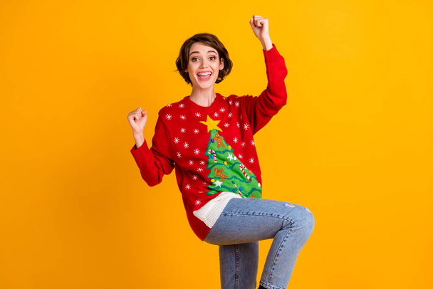 Photo of excited girl in christmas tree decor pullover sweater denim jeans raise fists x-mas newyear lottery win isolated over bright shine color background - Fotó, kép
