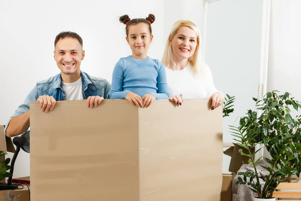 Happy family sitting on wooden floor. Father, mother and child having fun together. Moving house day, new home and design interior concept - Фото, изображение
