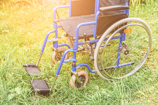 Lege rolstoel op gras in ziekenhuispark wachtend op patiëntenzorg. Ongeldige stoel voor gehandicapten geparkeerd buiten in de natuur. Handicap toegankelijk symbool. Gezondheidszorg medisch concept - Foto, afbeelding