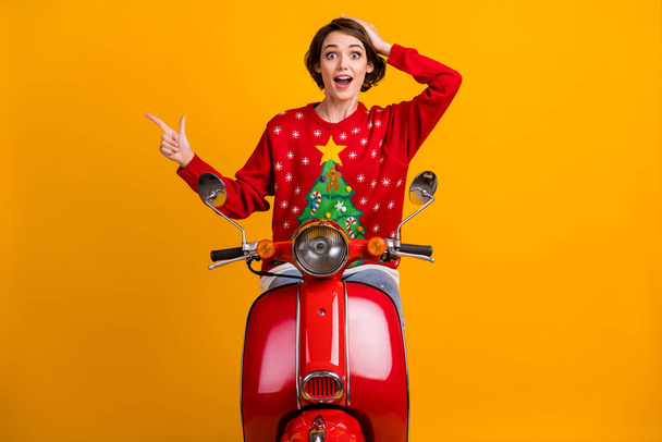 Excited girl in christmas tree decor sweater pullover point index finger copyspace impressed x-mas miracle fairy discounts drive motor bike isolated bright shine color background - 写真・画像