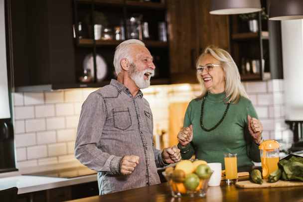 Senior couple enjoying while preparing lunch together in the kitchen - Photo, Image