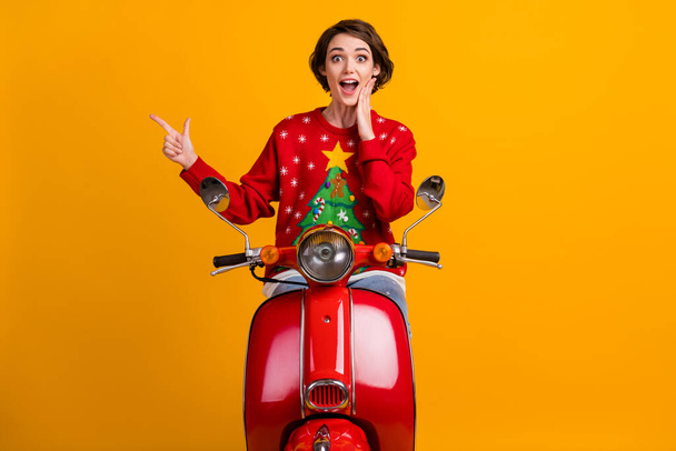 Photo of excited girl in christmas tree decor sweater jumper point finger copyspace x-mas magic discounts ride drive motor bike isolated over bright shine color background - Photo, Image