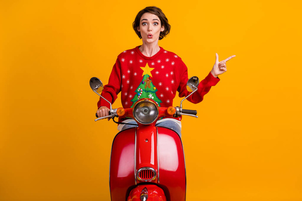 Photo of astonished girl drive ride red scooter point index finger miracle x-mas eve time promo wear christmas tree decor jumper pullover isolated over bright shine color background - Zdjęcie, obraz