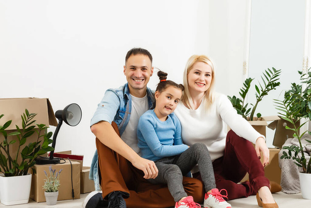 Happy family sitting on wooden floor. Father, mother and child having fun together. Moving house day, new home and design interior concept - Photo, image